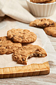 Delicious homemade chocolate chip cookies arranged on a wooden cutting board, with one cookie partially eaten