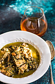 Delicious Georgian spring dish featuring stewed meat cooked with white wine, green plums, and assorted fresh herbs including tarragon, coriander, parsley, and green onions, served in a white bowl.