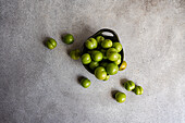 Bowl of organic green plums, essential in various Mediterranean cuisines, placed on a textured grey background