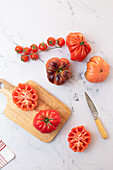 From above tomato salad preparation on wooden board with a knife and a selection of tomatoes