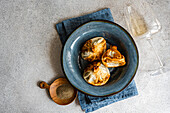 A rustic presentation of traditional Georgian khinkali, showcasing golden-browned dumplings arranged artfully on a blue ceramic plate A side of ground spice in a wooden bowl and a clear glass lay in the backdrop