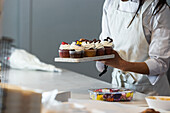 Gesichtslose weibliche Köchin steht mit verschiedenen veganen Cupcakes auf einem Brett in der Küche einer Backstube