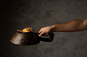 An artistic view of a hand arranging sushi on a rustic iron pan, emphasizing the elegance of sushi preparation in a moody lighting setup