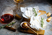 Artisanal Brie cheese paired with honey, fresh rosemary, and glasses of red and white wine, set for a refined tasting.