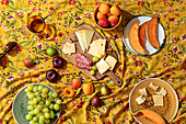 A vibrant, inviting summer picnic setup, featuring an assortment of fruits, cheeses, and charcuterie on a floral yellow tablecloth.