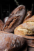 Eine Auswahl an frischem, knusprigem Sauerteigbrot, stolz handgemacht, in einem rustikalen Weidenkorb arrangiert.