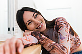 Positive female leaning on hand while sitting at counter and chilling in bar during weekend