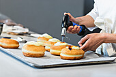 Unrecognizable crop chef caramelizing sugar cream on sweet Berliners with gas torch while preparing vegan dessert in bakehouse