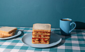 Peanut Butter and Jelly sandwich served on a blue plate , a cup of an american coffee and some bread slices in a blue background