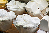 Glass bowls filled with different types of fresh white cheese displayed at a market