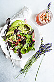 Fresh garden salad with mixed greens, avocado slices, cucumbers, tomatoes, radishes, olives, sesame seeds, and a side of lavender.