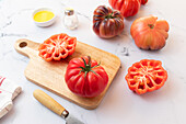 From above tomato salad preparation on wooden board with a knife, salt, olive oil and a selection of tomatoes