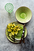 Top view of a sophisticated table setting featuring bright green ceramic dishes, complemented by sleek cutlery and a decorative glass on a textured surface.