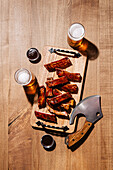 A rustic barbecue setting with juicy, grilled ribs laid out on a wooden cutting board, accompanied by two glasses of frothy beer and a unique cleaver