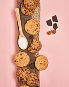 Assorted homemade chocolate chip cookies with a spoon of sugar and dark chocolate pieces, artfully arranged on a rustic wooden board