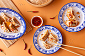 A vibrant top-view of traditional Asian dumplings on ornate blue and white plates, accompanied by a spicy dipping sauce and chili peppers on a burnt-orange background