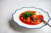 Authentic Ukrainian borscht served in a white bowl with blue trim, garnished with fresh parsley and a dollop of sour cream on top