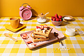 A vibrant breakfast scene with crispy waffles topped with cream and fresh-cut strawberries, paired with coffee and milk, all set against a sunny yellow backdrop