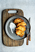 Overhead view of golden brown potato american pancakes served with sour cream on a gray plate, with rustic wooden background.