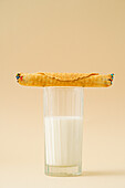 A crispy waffle roll filled with condensed milk resting atop a full glass of milk, set against a pastel background.