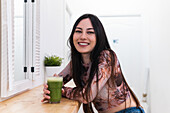 Positive female sitting looking at counter with green smoothie and chilling in bar during weekend