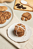 A charming presentation of chocolate chip cookies, tied with twine on a decorative white plate, with more cookies and ingredients nearby