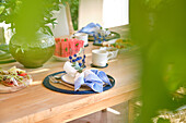 Through a frame of lush foliage, a serene breakfast table on a terrace is glimpsed, promising a peaceful start to the day