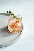 A crafted vodka tonic cocktail adorned with grapefruit and rosemary, resting on a textured tray for an upscale serving experience