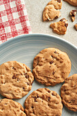 Golden-brown chocolate chip cookies on a light blue ceramic plate, with a red checkered napkin alongside on a textured surface