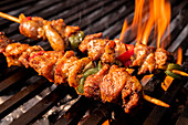 Succulent Mexican barbecue skewers with chicken, bell peppers, and onions grilled over flaming charcoal, showcasing mouth-watering char and vibrant colors.