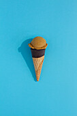 A vibrant coffee ice cream scoop sits atop a classic waffle cone against a blue background, casting a playful shadow