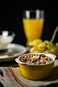 Studio photo of a nutritious breakfast set including orange juice, grapes, and a bowl of cereals, captured in a sharp foreground focus against a blurred backdrop.