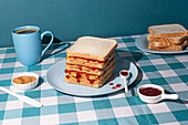 Stack of peanut butter and Jelly sandwiches just prepared , with a cup of an american coffee and some bread slices in a blue background