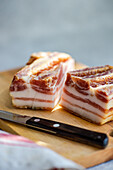 A close-up view of thick, sliced lard or bacon on a wooden cutting board next to a kitchen knife.