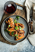 Top view succulent roasted chicken wings in a spicy sauce garnished with fresh coriander leaves, served alongside a refreshing glass of cherry cocktail.