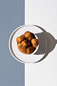 A minimalist composition of golden-brown croquettes served on a white plate, captured from above, showcasing the interplay of light and shadows