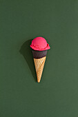 A vibrant Strawberry ice cream scoop sits atop a classic waffle cone against a green background, casting a playful shadow