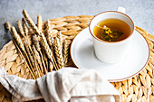 A cup of black tea with a tea bag alongside wheat sheaves and a woven placemat, evoking a warm and rustic tea time ambiance.