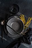 from above elegant black tableware set on a dark surface, complemented by a vibrant touch of yellow mimosa flowers for a contrast.