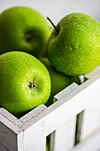 Vibrant green apples with a fresh dewy texture are neatly packed in a rustic white wooden crate, showcasing their ripe and juicy appearance ideal for healthy snacking