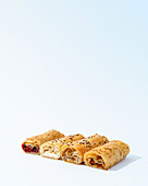 A selection of flaky pastry rolls with various fillings, garnished with seeds, on a clean white background.