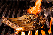 A succulent pork chop is expertly grilled over a fiery barbecue, capturing the essence of traditional Mexican home cooking. The flames lick the meat, enhancing its flavors.