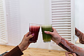 Cropped unrecognizable multiethnic female friends sitting at counter and drinking refreshing smoothie while chilling in bar