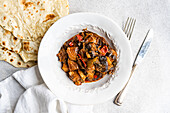 Ein schmackhafter Gemüseeintopf mit Auberginen, Tomaten, Kartoffeln, Paprika, Zwiebeln, Knoblauch und Basilikum, serviert mit hausgemachtem Fladenbrot auf einem weißen Teller