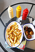 From above enjoying a leisurely day at home with a serving of crispy french fries and tasty falafel balls, conveniently placed on a modern glass coffee table, accompanied by condiment dispensers.