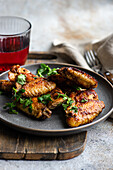 Roasted chicken wings in a spicy sauce, garnished with fresh coriander, presented on a plate with a glass of cherry cocktail on a rustic wooden table.