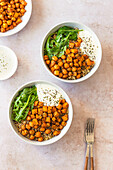 Two bowls of nutritious quinoa salad topped with spiced chickpeas, roasted sweet potato cubes, fresh arugula, and a dollop of creamy yogurt sauce, garnished with dried herbs