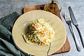 Top view of a healthy organic cabbage and carrot salad drizzled with olive oil, served on a decorative ceramic plate, accompanied by a glass bottle of olive oil and utensils on a textured surface.