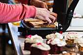 Side view of crop anonymous cook preparing tasty vegan sandwiches in panini press placed on table in bakehouse