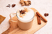 Von oben: Chai Latte mit schaumiger Milch, Sternanis und Zimtstangen auf einem Holzbrett mit frischen Zutaten